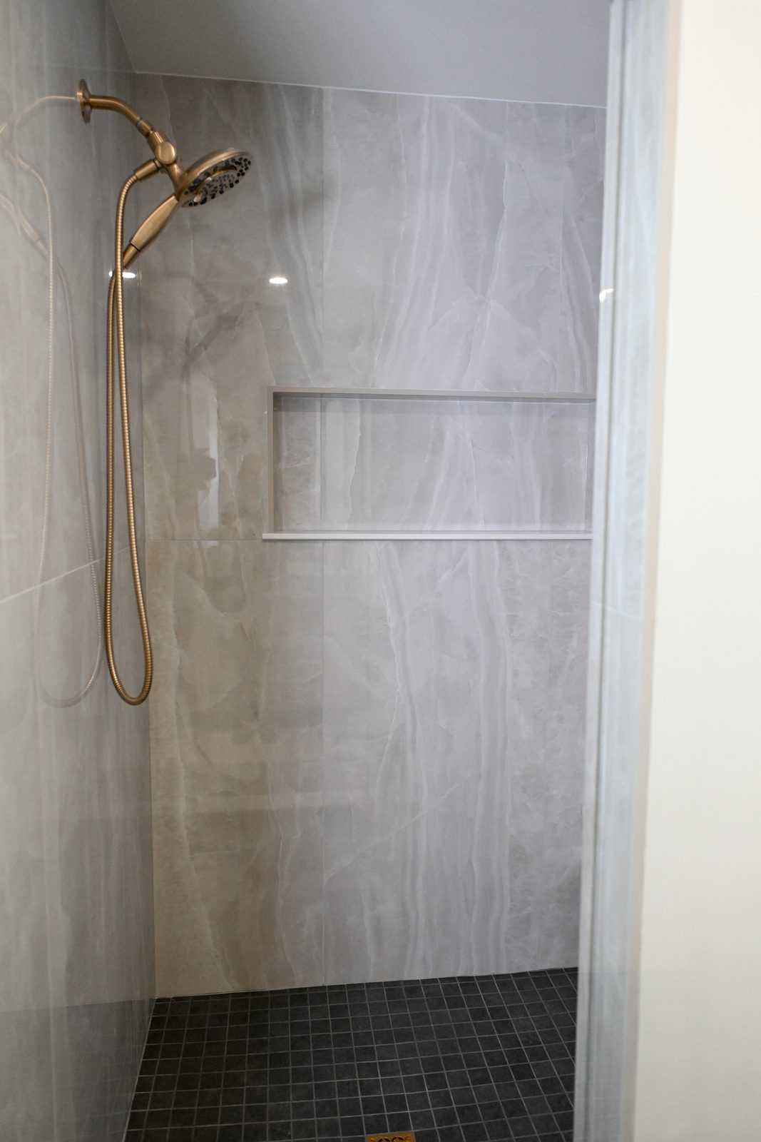 Tiled basement shower with niche and brass shower head Westfield IN